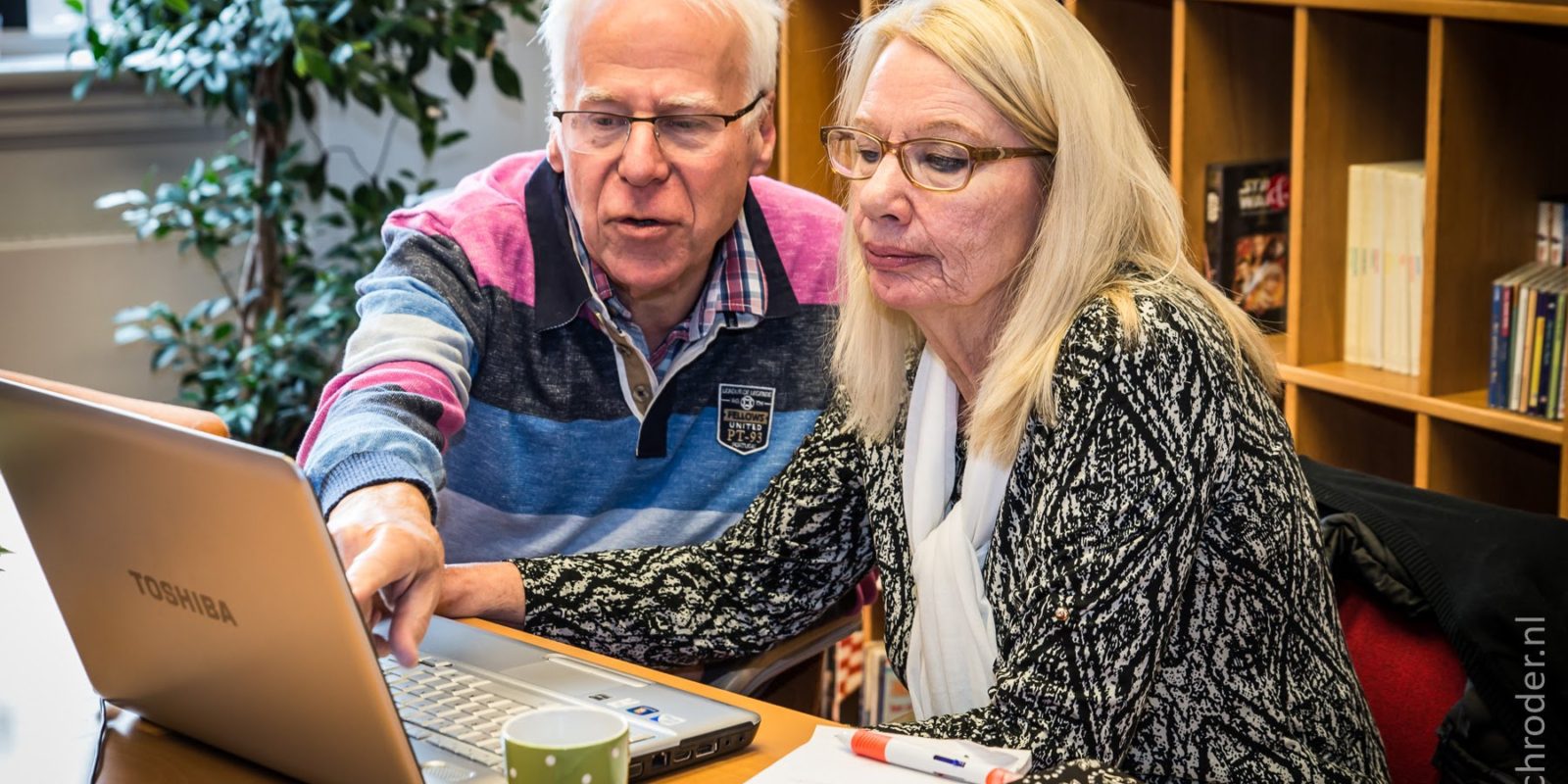 Oudere man en dame aan tafel zitten achter laptop