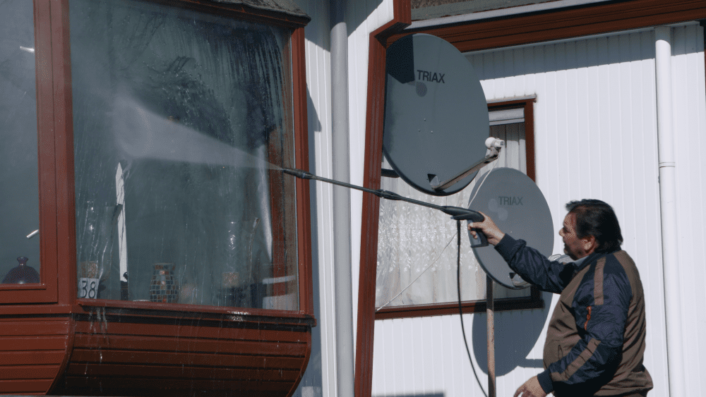 Man die met een waterspuit zijn woonwagen schoonmaakt.