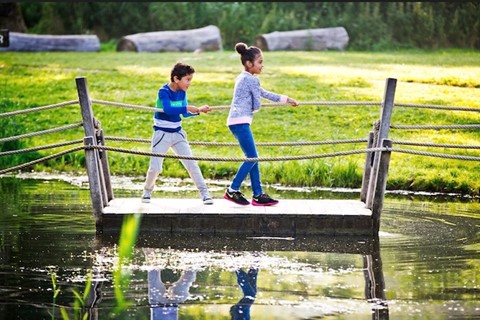 Twee kinderen spelen op een houten bruggetje in de natuur.